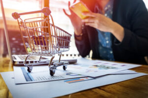 Mini Carrinho de compras em cima de uma mesa com notebook e uma mulher usando o celular